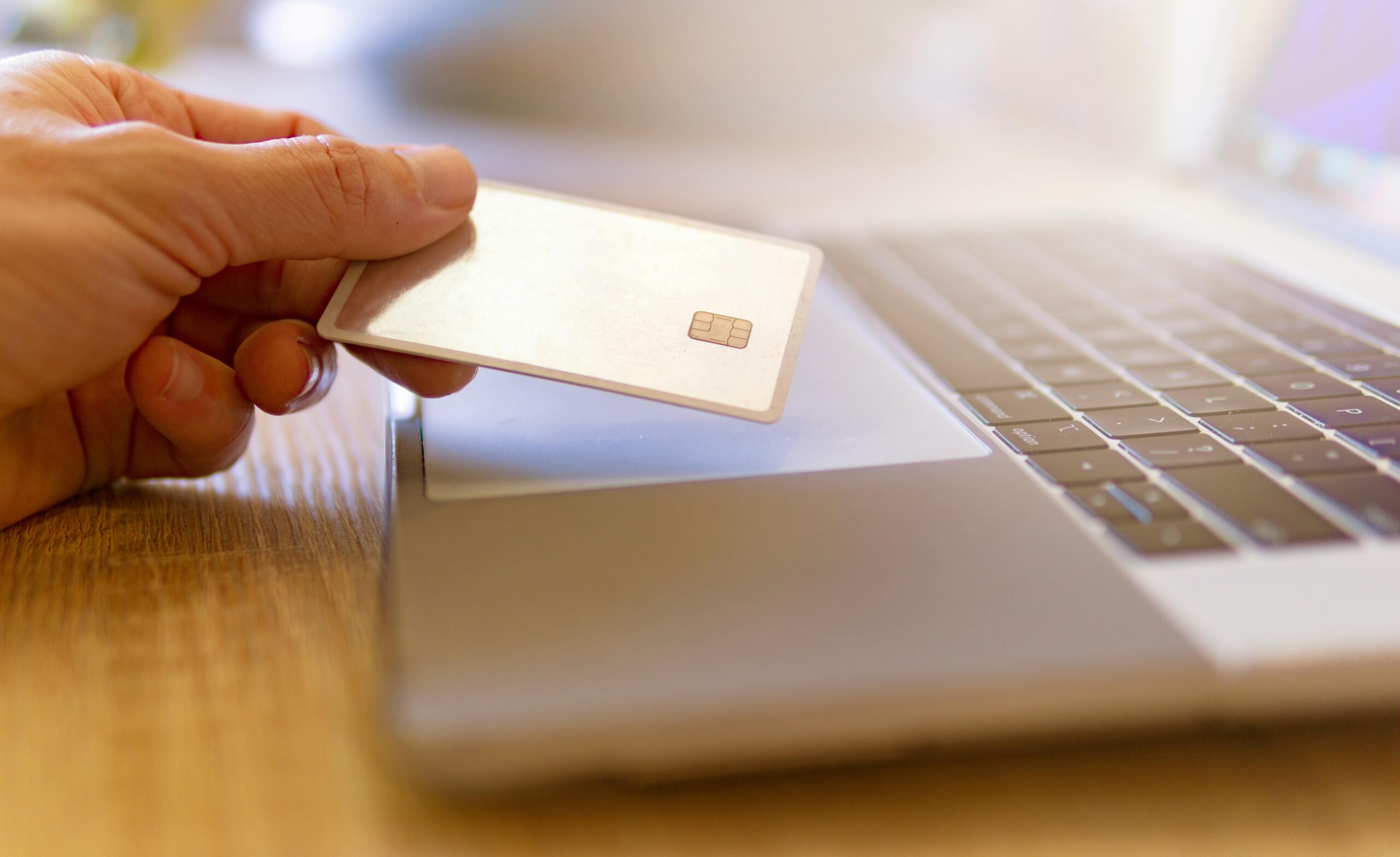 Hand holding a generic credit card near a laptop for a credit utilization article